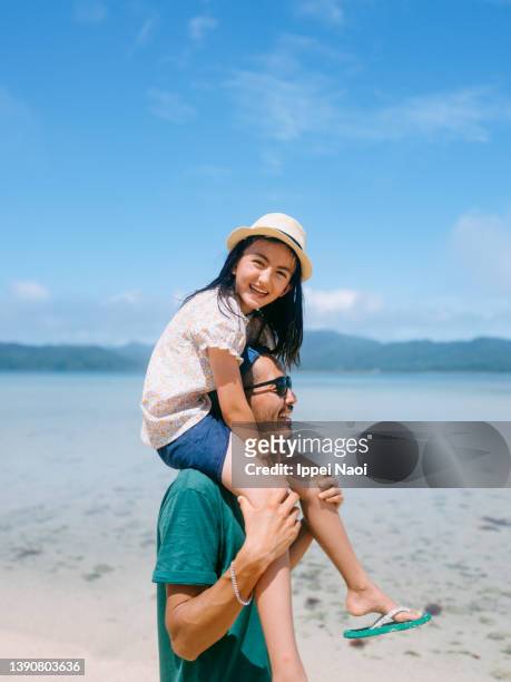 father carrying young daughter on shoulders on beach - mann mit kind auf den schultern stock-fotos und bilder