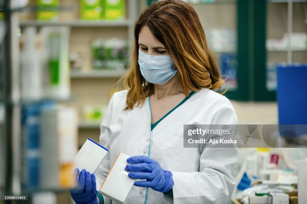 Female pharmacist in the pharmacy holding a medicine.