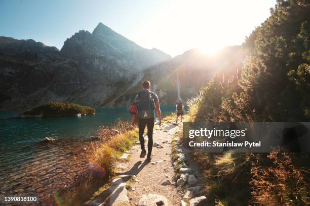 two men with backpacks trekking along mountain lake at sunset - tatra stock-fotos und bilder