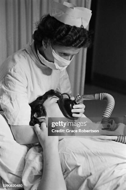 Midwife helps a pregnant woman in labor to breath through a pain relief breathing apparatus for nitrous oxide at a birth centre, UK, 1956. Original...