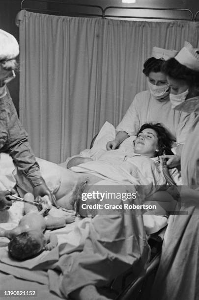 Woman is seen with medical team of midwives as an obstetrician cut the umbilical cord of her newborn baby right after childbirth, UK, 1956. Original...