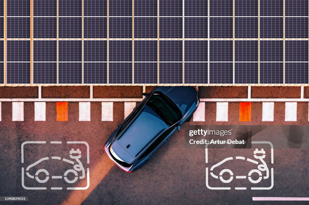 Aerial view of electric car parking in charging station with solar panels.