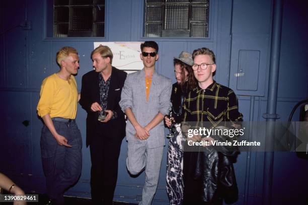 British New Wave band Modern English pose against a blue background, on which is a poster for the band, circa 1985.