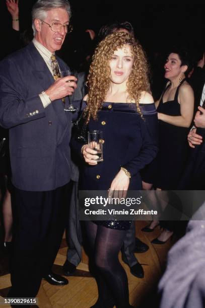 American actress and singer Bernadette Peters wearing a midnight blue off-the-shoulder jacket with brass buttons and a black sequin miniskirt,...