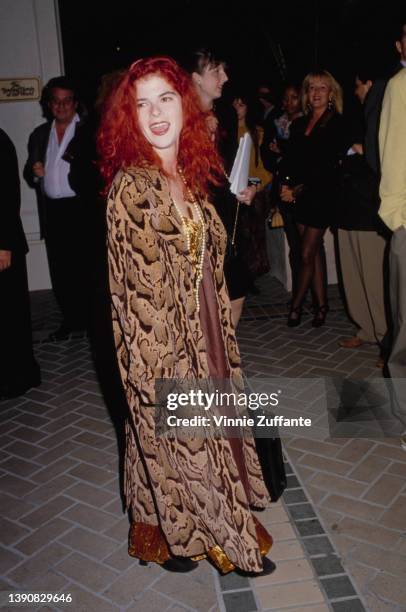 American actress Olivia Barash, wearing a long snakeskin-effect coat over an orange velvet evening gown, attends a party hosted by Entertainment...