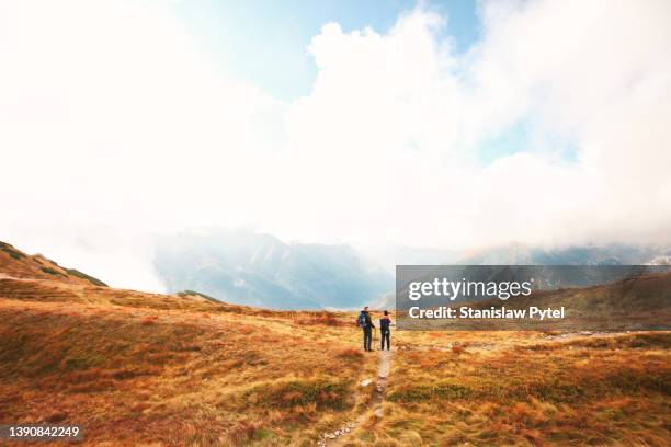 two men in trekking clothes standing against clouds and mountains at autumn - tatra national park stock pictures, royalty-free photos & images