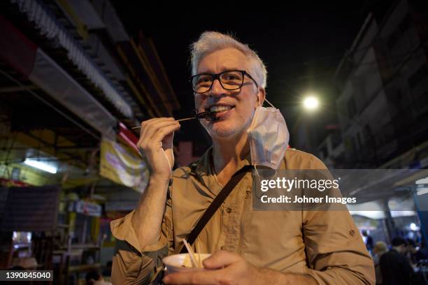 portrait of smiling senior man eating street food - eating scorpion stock pictures, royalty-free photos & images