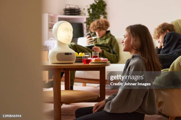 siblings sitting in living room and using robotic voice assistant - bionics research stock-fotos und bilder