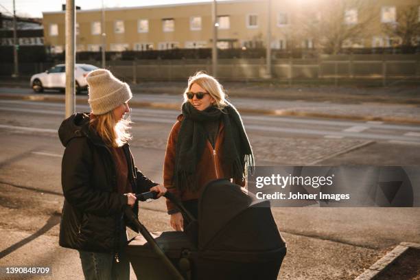 mothers with baby stroller walking along street - mother stroller stock pictures, royalty-free photos & images