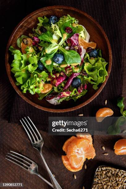 frischer veganer salat mit gemischtem grün, blaubeeren, mandarinen und sonnenblumenkernen - kopfsalat stock-fotos und bilder