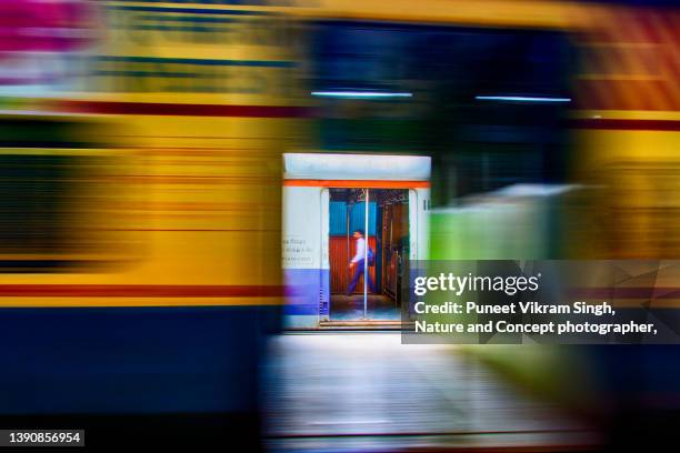 a daily commuter in blurred motion walks on the platform while another local train passes by in mumbai - office action foto e immagini stock