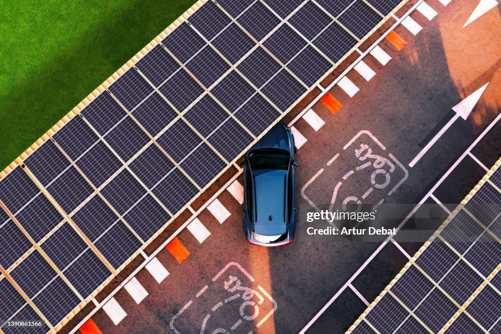 Aerial view of electric car parking in charging station with solar panels.