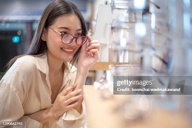 young happy woman choosing eyeglasses in optician store. - visual impairment - fotografias e filmes do acervo