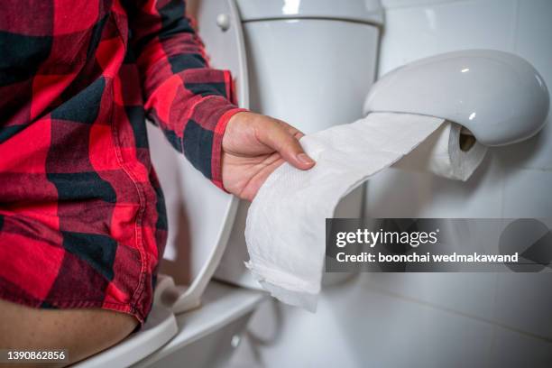 a man holding toilet paper while defecating in the bathroom. - emorroidi foto e immagini stock