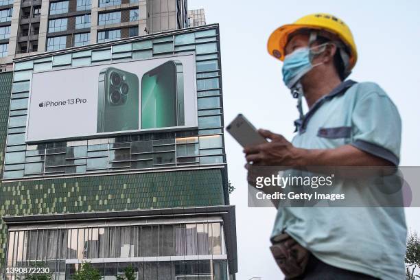 The construction worker wearing a mask passes a large outdoor advertisements for the Apple iPhone 13 Pro near Wuhan International Plaza on April 11,...