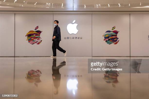 People wear masks while passing a board of the new Apple store in Wuhan International Plaza on April 11, 2022 in Wuhan, Hubei province, China....
