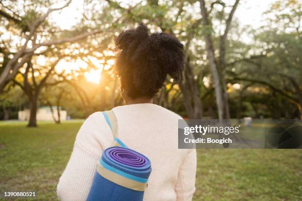 rearview of african american woman walking with a yoga mat in the park - showus yoga stock pictures, royalty-free photos & images