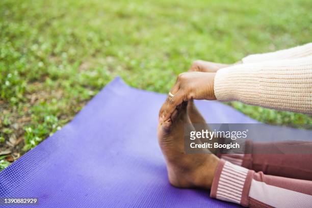 close up of a black woman's hands holding feet in a yoga pose - touching toes stock pictures, royalty-free photos & images
