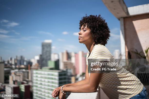 young woman breathing with eyes closed on apartment's balcony - breathe stock pictures, royalty-free photos & images
