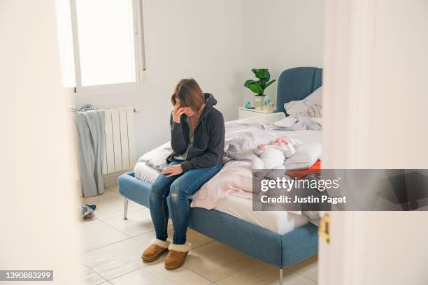 upset mature woman holding her face as she sits on her bed with her baby - postnatal depression - depressed mother stockfoto's en -beelden