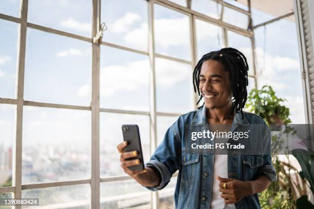 young man on a video call on the mobile phone at home - mms stockfoto's en -beelden