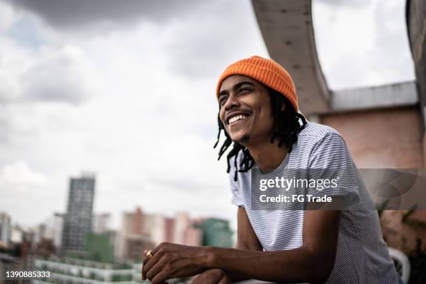 joven mirando hacia otro lado contemplando en el porche del apartamento - cruzar los dedos fotografías e imágenes de stock