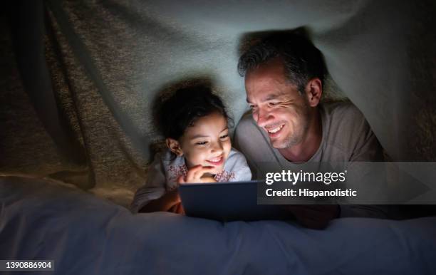 vater und tochter lesen ein buch im bett auf einem tablet-computer - livestreaming stock-fotos und bilder