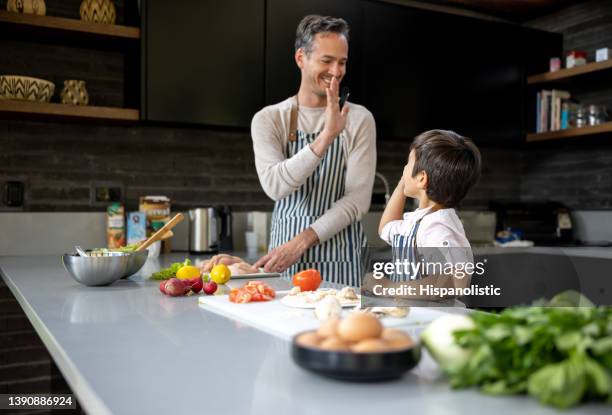 happy father and son cooking togheter and high-fiving - quarantine cooking stock pictures, royalty-free photos & images