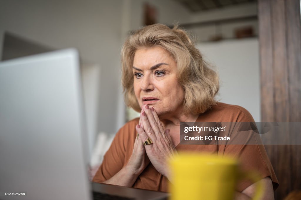 Shock senior woman using the laptop at home