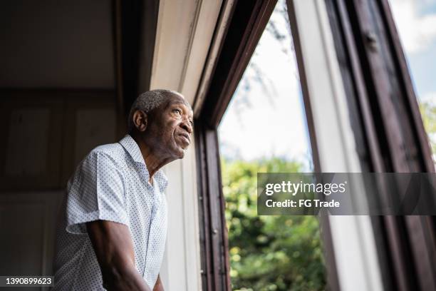 uomo anziano che contempla guardando attraverso la finestra - guardare fuori dalla finestra foto e immagini stock