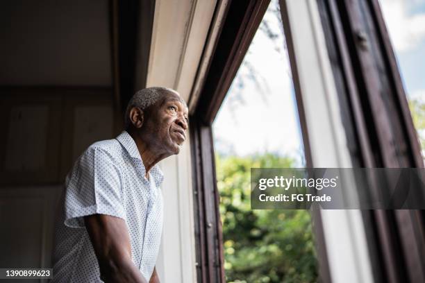 senior man contemplating looking through the window - distraught elderly stock pictures, royalty-free photos & images