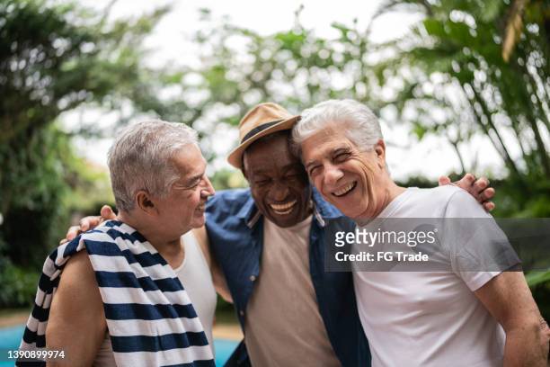 senior men embracing on a pool party - friendship stock pictures, royalty-free photos & images
