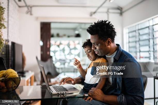 vater, der den laptop mit sohn zu hause benutzt - african american dad stock-fotos und bilder