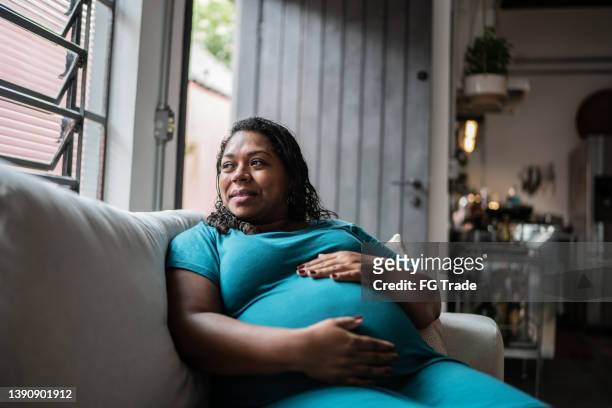 schwangere frau berührt ihren bauch und denkt zu hause nach - hochschwanger stock-fotos und bilder
