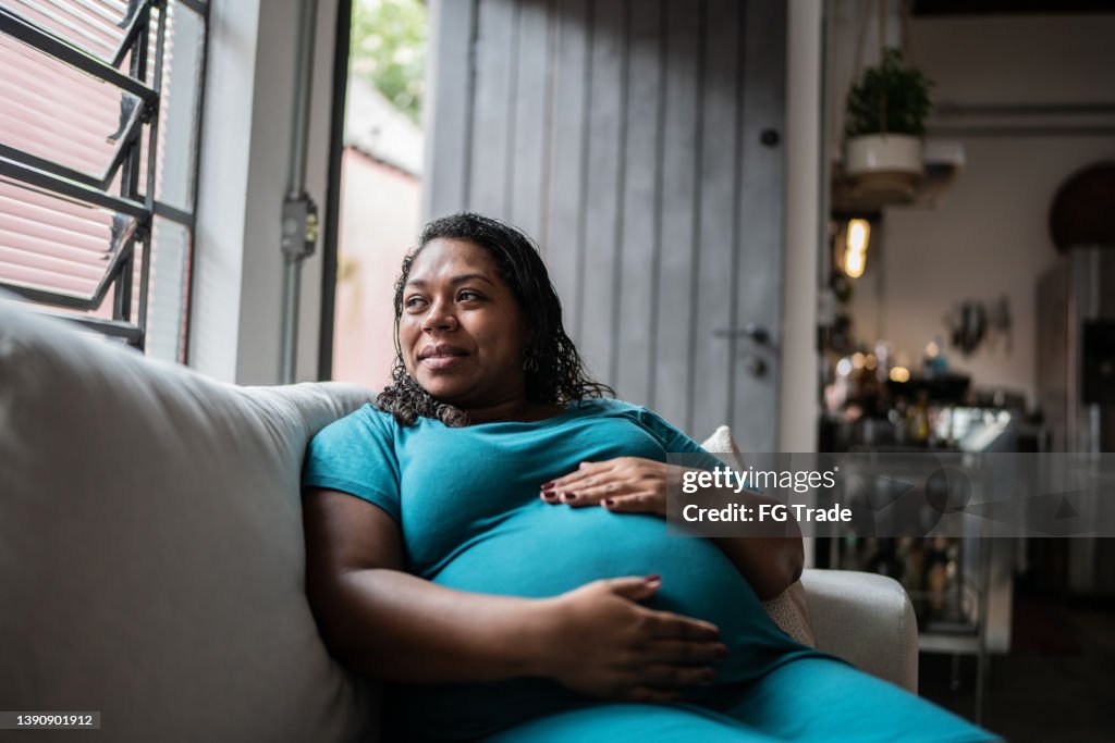 Pregnant woman touching her belly and contemplating at home