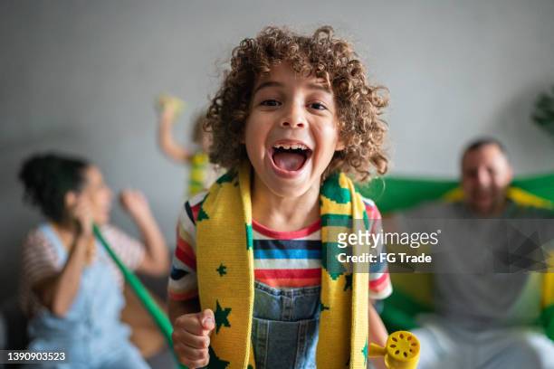 portrait of a boy cheering for brazilian soccer team with family at home - boys soccer stock pictures, royalty-free photos & images