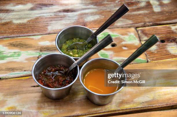 three stainless steel ramekins of salsas on a recycled wood outdoor cafe table - salsa verde, mango, and chimichurri - ramequin photos et images de collection