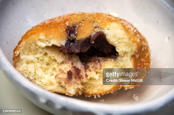 red bean paste filled berliner doughnut with a missing bite in a small serving bowl - beignet fourré photos et images de collection