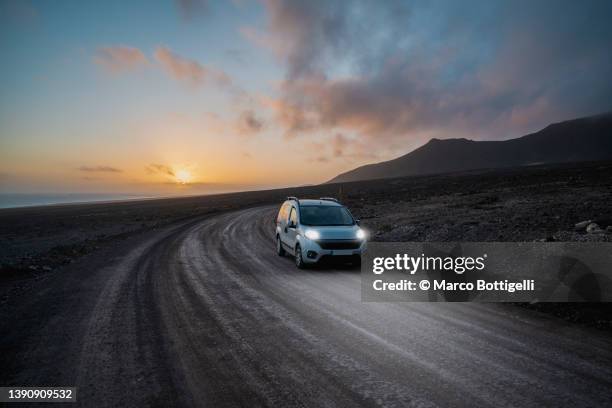 car driving on dirt road at sunset in lanzarote, spain - highway dusk stock pictures, royalty-free photos & images