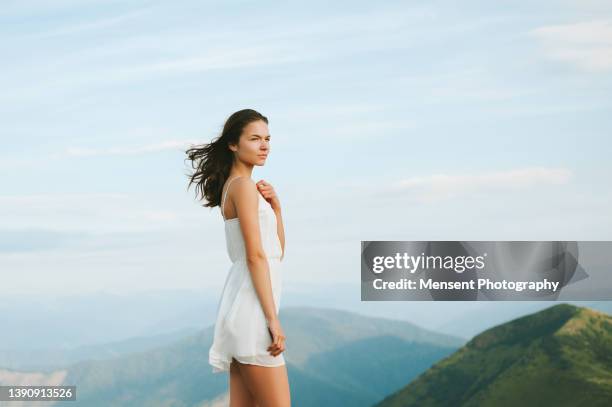 one woman traveler standing in white dress on mountain against cloudy sky - white dress back stock pictures, royalty-free photos & images