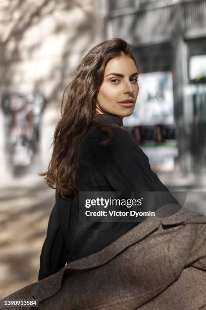 cute girl with brown eyes dressed in a brown coat and a black shirt looks curiously at the camera. - woman portrait brown hair stock pictures, royalty-free photos & images