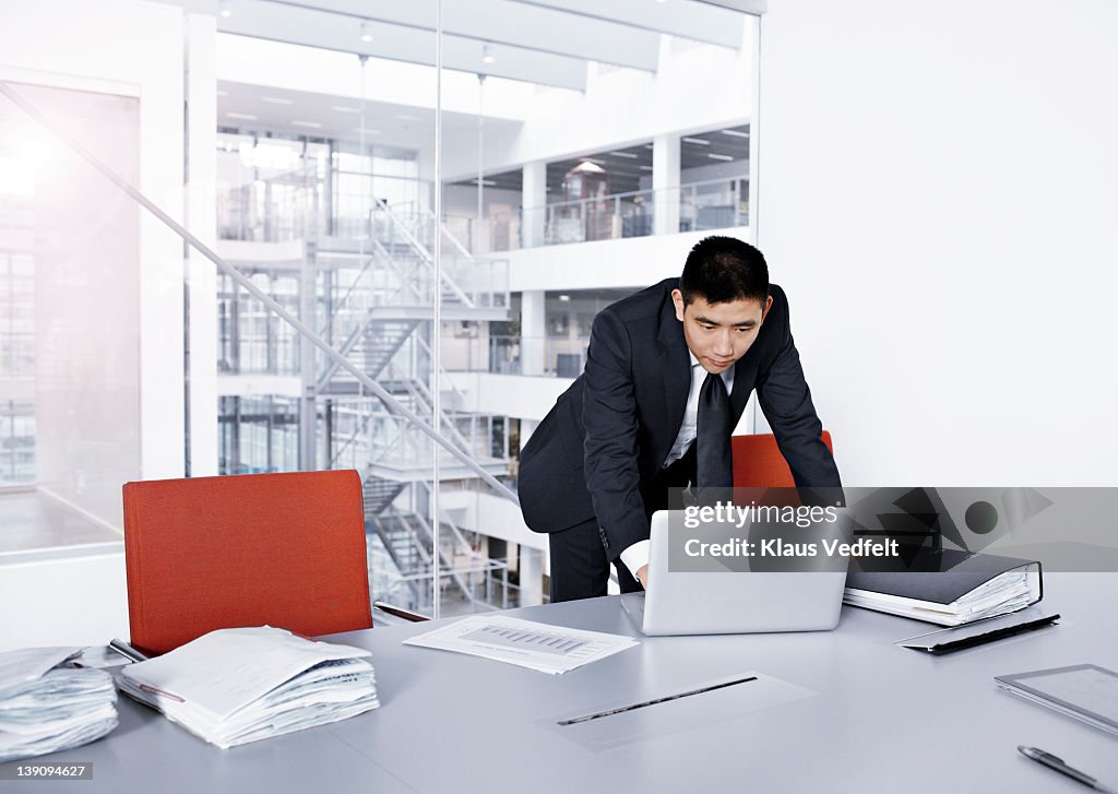 Asian businessman standing up working at laptop