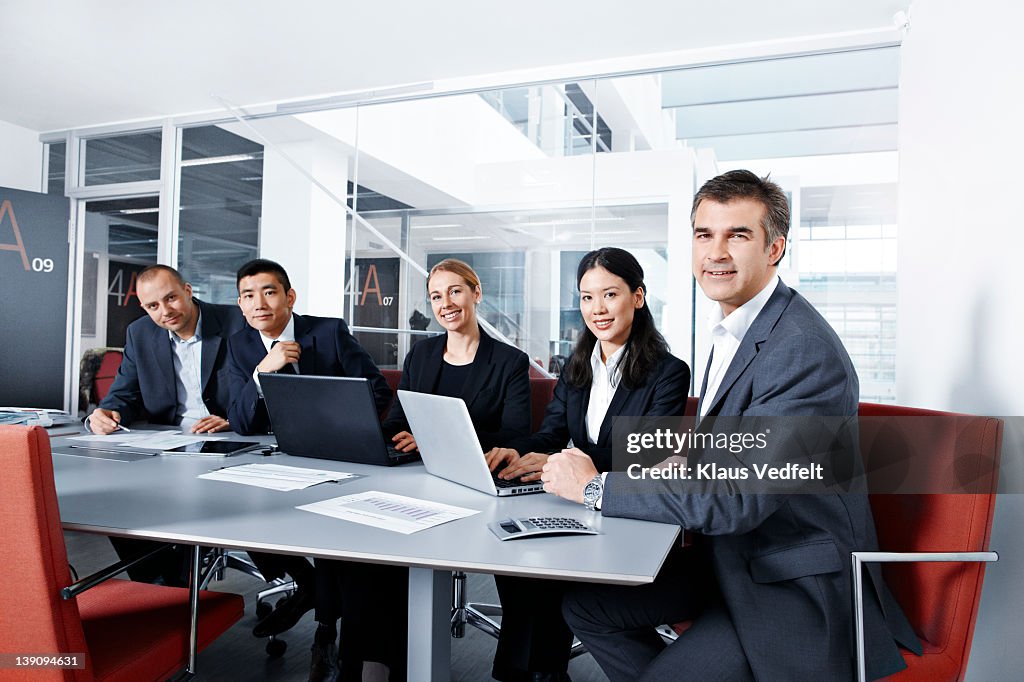 5 businesspeople at a meeting looking in camera