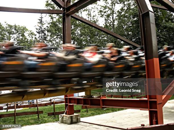 travel photography, roller coaster ride with side view of high speed passenger carriage showing people enjoying the ride on dramatic sky background. selective focus - beer mat stock pictures, royalty-free photos & images