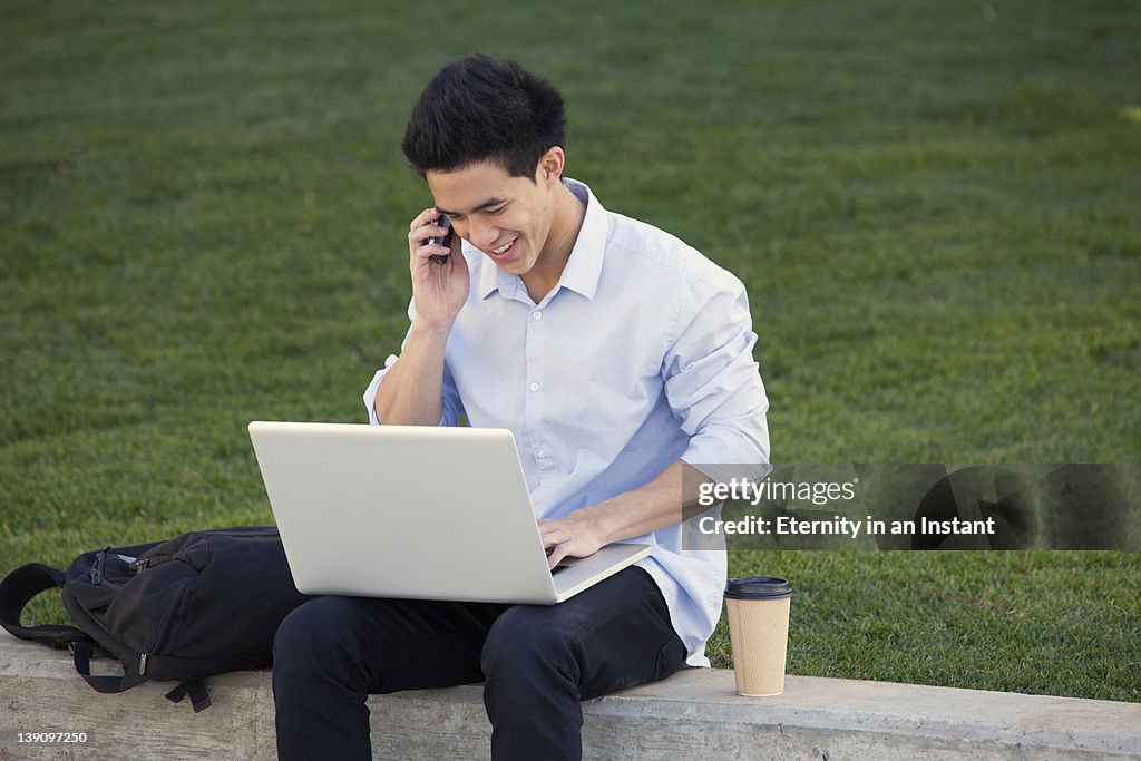 Young man working on laptop talking on phone