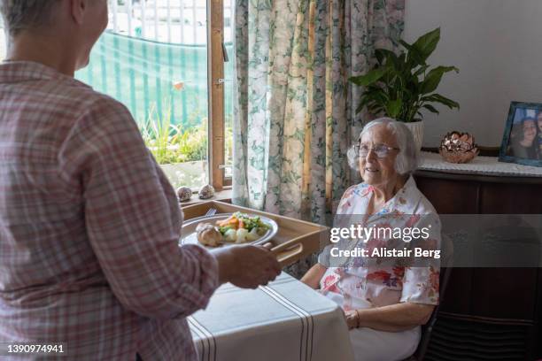 mature female carer serving lunch to a senior woman - volunteer aged care stock pictures, royalty-free photos & images