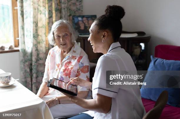 community nurse using a digital tablet to record details of senior patient - visite stock-fotos und bilder