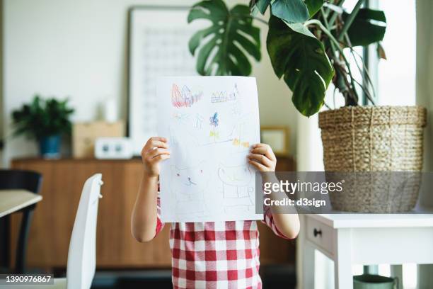 little asian girl holding up a hand drawn picture, showing her drawing of animals at home. developing a habit, hobbies, creativity and art ideas - kid holding crayons stock pictures, royalty-free photos & images