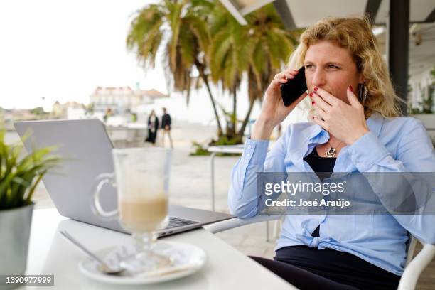 woman working from a beach terrace, on a smartphone call - pessoas notebook stock pictures, royalty-free photos & images