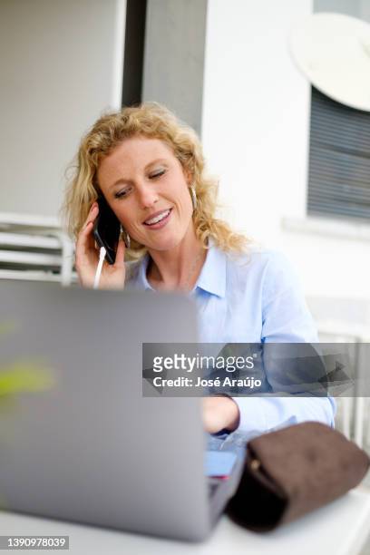 woman working from a beach terrace, on a smartphone call - pessoas notebook stock pictures, royalty-free photos & images